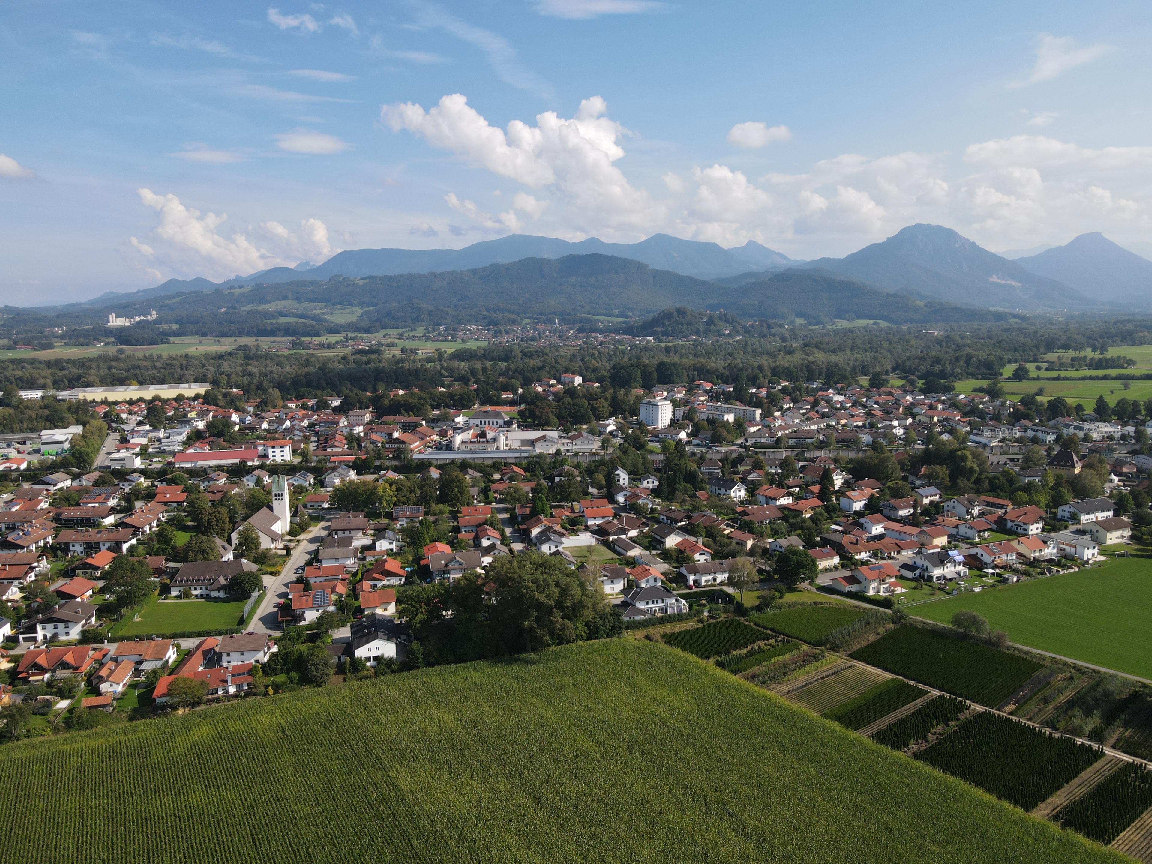 Luftaufnahme von Raubling mit Wohngebieten, Feldern und Bergpanorama im Hintergrund.