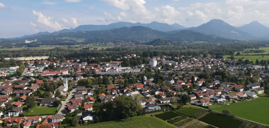 Luftaufnahme von Raubling mit Wohngebieten, Feldern und Bergpanorama im Hintergrund.