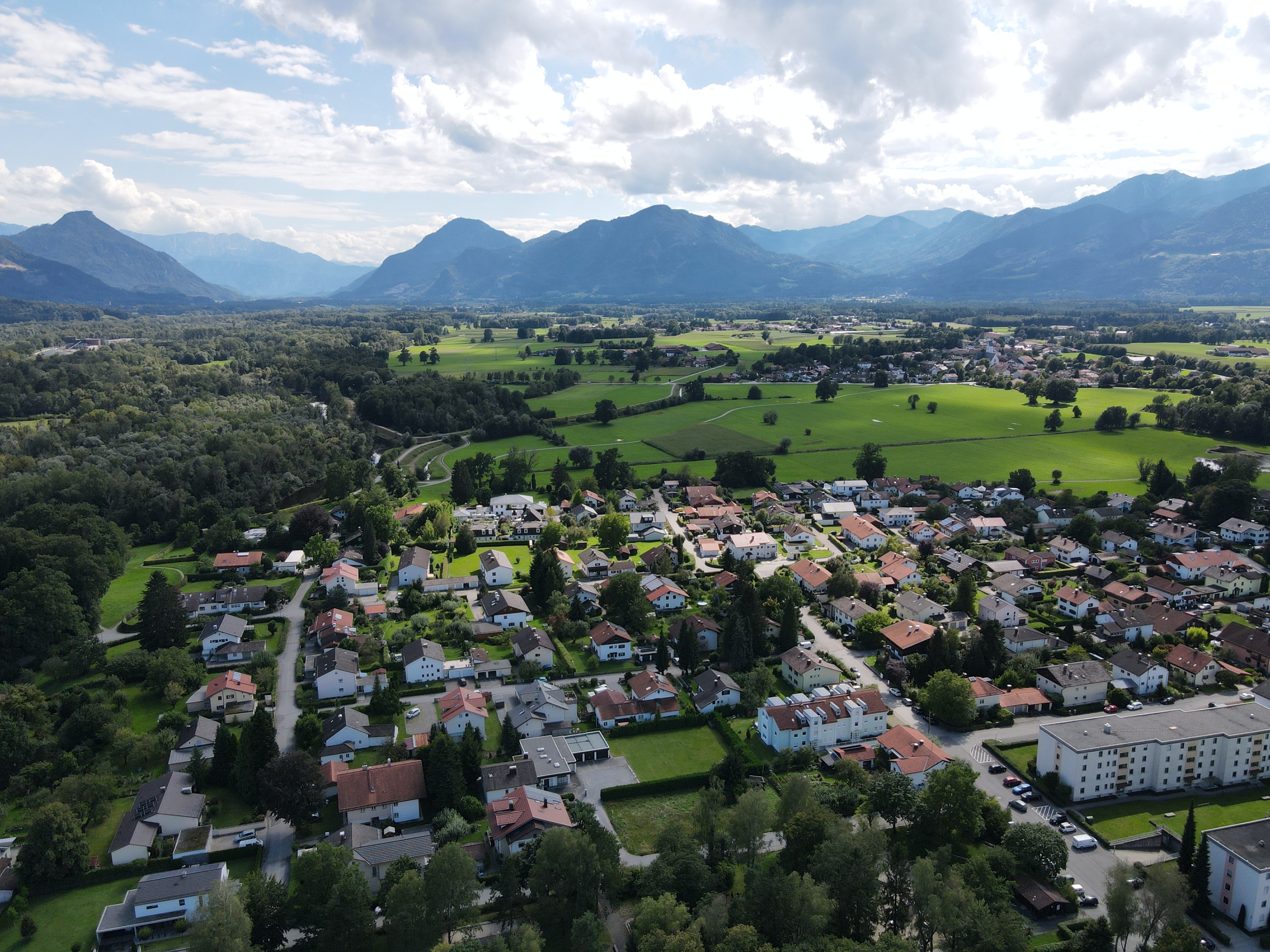 Luftaufnahme von Raubling mit Wohngebieten, Feldern und Bergpanorama im Hintergrund.