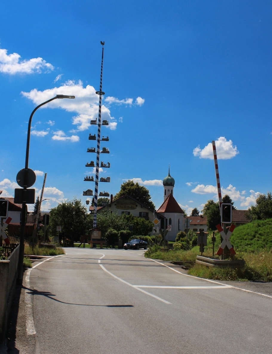 Ländliche Straße an einem Bahnübergang unter blauem Himmel.