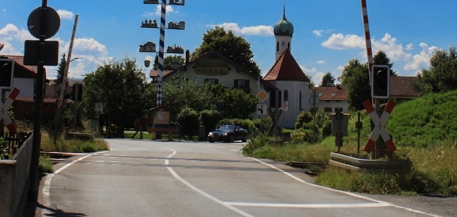 Ländliche Straße an einem Bahnübergang unter blauem Himmel.