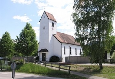 Weiße Kirche mit kleinem Turm und Satteldach, umgeben von Bäumen